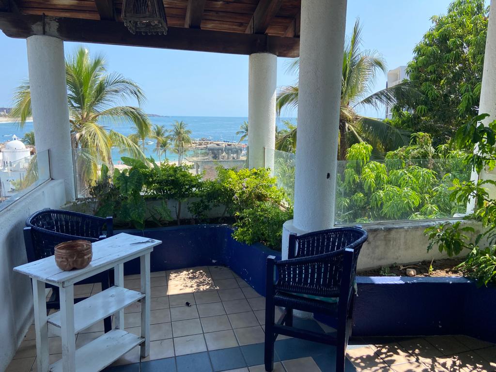 Rooftop terrace with blue chairs and a sea view through palm trees at MayFlower Hotel & Hostal