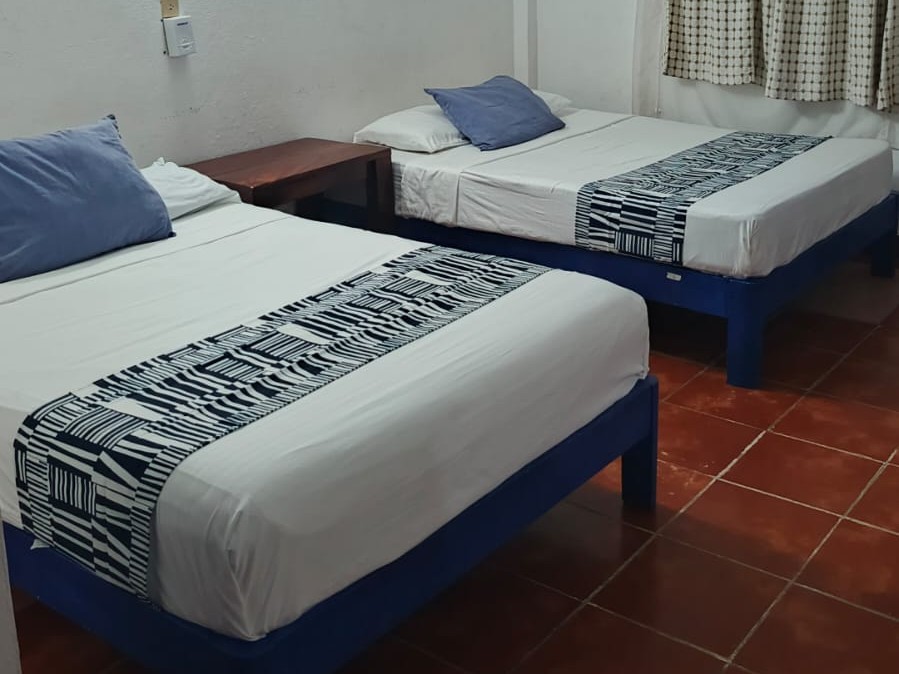 Private room at MayFlower with two beds on blue frames, striped runners and a terracotta tile floor